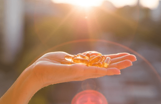 An open hand holding golden omega-3 capsules in warm backlit sunlight